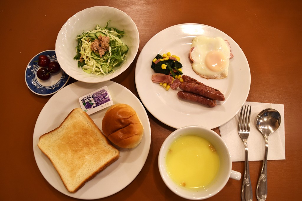 洋食 (パン・コーンスープ・サラダ・ウインナー・ほうれん草とベーコンの炒め物・目玉焼き・果物)